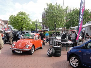 Das Foto zeigt einen roten Oldtimer sowie einen Stand, der sich mit Reifen beschäftigt.