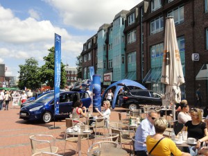 Neben den ausgestellten Autos am Tibarg sitzen Besucher in einem Café bei Essen und Trinken.