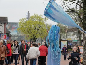 Eine blau-gekleidete Künstlerin mit einer großen blauen Windfahne ist ein Hingucker für die spazierenden Besucher.