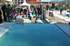Das Foto zeigt vordergründig das blaue Wasser des Brunnens, im Hintergrund Kinder und Erwachsene.