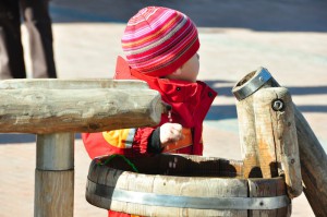 Ein Kind spielt mit dem Wasser eines hölzernen Brunnens