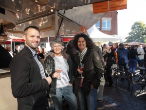 Drei Besucher genießen ihr Glas Wein und schauen lächelnd in die Kamera.