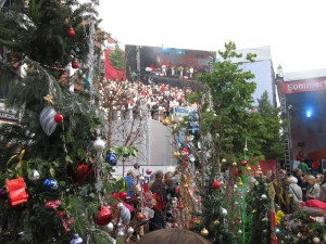 Im Vordergrund befinden sich weihnachtlich geschmückte Bäume, hintergründig die gut besuchte Bühne zur NDR Sommertour.