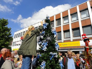 Eine Frau schmückt in der Zuschauermenge einen Tannenbaum mit blauen und silbernen Schleifen.