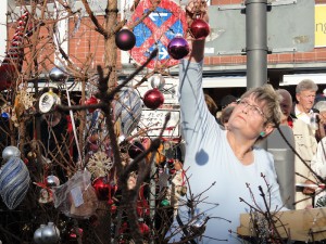 Eine Frau schmückt einen kahlen Baum mit bunten Weihnachtsbaumkugeln.