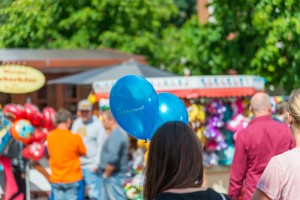 Das Foto zeigt eine Frau von hinten mit zwei blauen Ballons in der Hand vor dem bunten Treiben beim Tibargfest 2016 in Hamburg-Niendorf