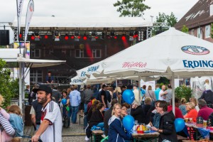 Das Foto zeigt Menschen sitzend auf Bierbänken vor der Bühne beim Tibarg mit Speisen und Getränken