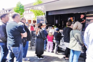 Das Foto zeigt auf ihr Essen wartende Menschen vor einem Food Truck auf dem Tibarg Foodtruck Festival 2016 in Hamburg-Niendorf am Tibarg