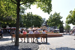 Ein Platz mit vielen Menschen auf dem Tibarg. Es sitzen Menschen auf einer Bank und schauen sich das bunte Treiben an.