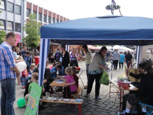 Unter einem blauen Pavillon basteln Kinder unter Anleitung von Betreuerinnen.