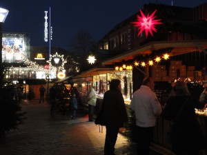 Stände auf dem Weihnachtsmarkt mit weihnachtlicher Beleuchtung aus Lichterketten und Sternen.