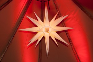 Ein weißer Weihnachtsstern hängt im Inneren eines rot-beleuchteten Zeltes.