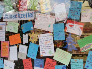 An einer Fensterscheibe hängen zahlreiche bunte Wunschzettel von Kindern.