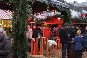 Unter einem mit Tannenzweigen beschmückten Dach sitzen Besucher auf Hochstühlen.