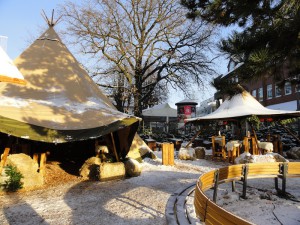 Das Foto zeigt den leicht verschneiten Weihnachtsmarkt bei Tag mit Strohballen, Sitzgelegenheiten und Tipi-Zelt.