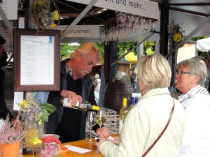 Ein Verkäufer schenkt an einem Stand zwei Gläser Weißwein für zwei Frauen ein.