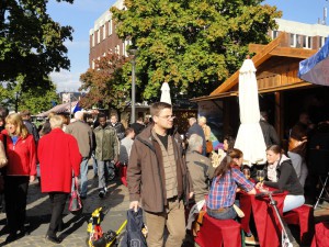 Buntes Treiben beim Weinfest: Einige Besucher trinken sitzend Wein, andere schlendern an den Ständen entlang.