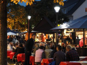 Besucher sitzen am Abend an Tischen zusammen und genießen Essen und Getränke am beleuchteten Tibarg