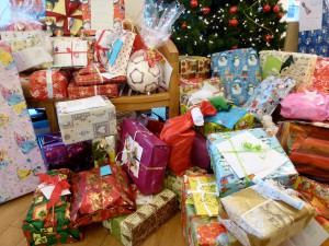 Zahlreiche, bunt verpackte Geschenke liegen auf einer Bank und auf dem Boden unter einem Tannenbaum