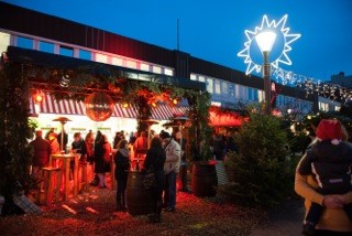 Blick auf einen beleuchteten Weihnachtsmarktstand mit Tannenzweigen-Dekoration